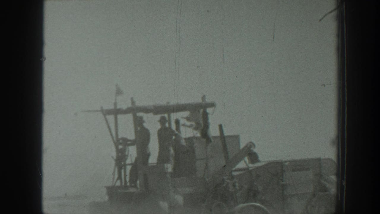 A tractor and farm implement move through haze with men standing on the machinery.