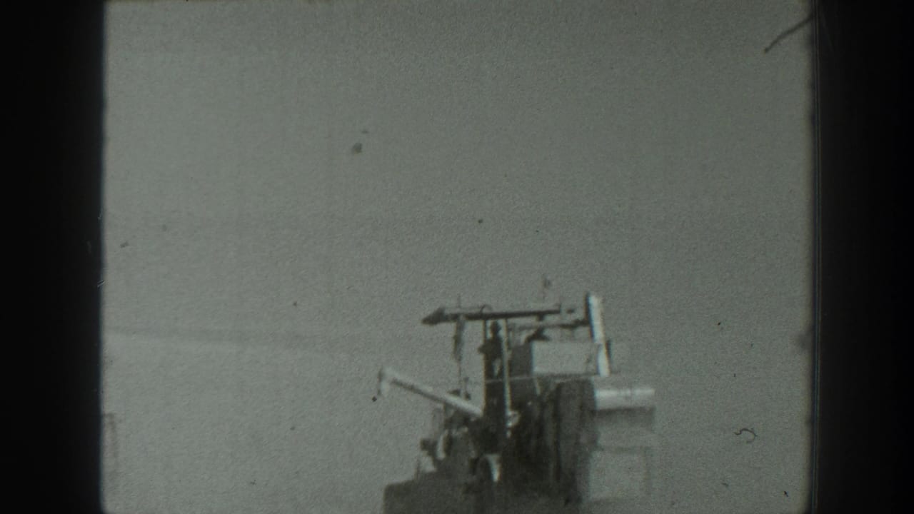 Artillery piece or field equipment with a few figures nearby on open terrain.