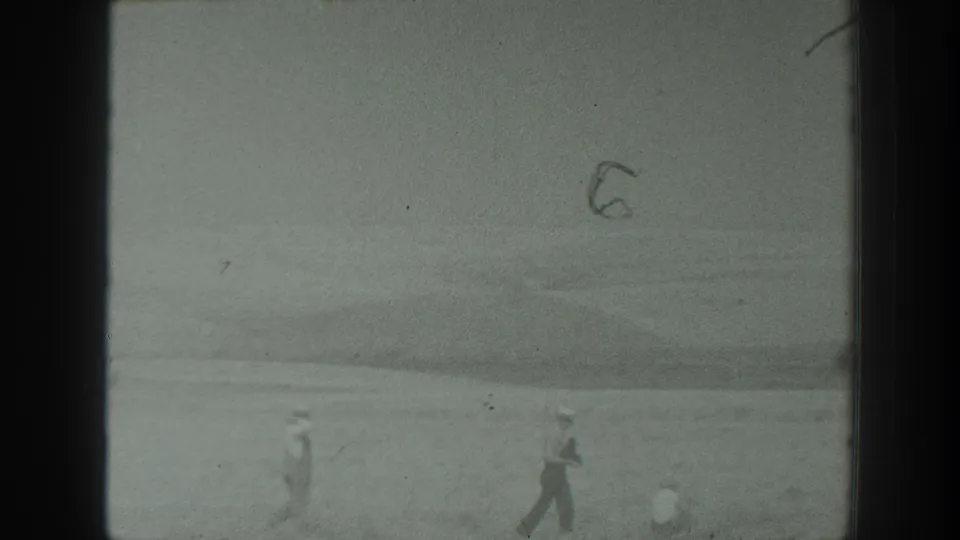 1939 California footage frame with distant travelers crossing a broad open area, one apparently handling a camera.