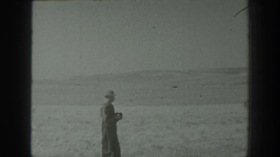 1939 California home-movie frame showing a man in a hat pausing with a camera against a broad natural backdrop.