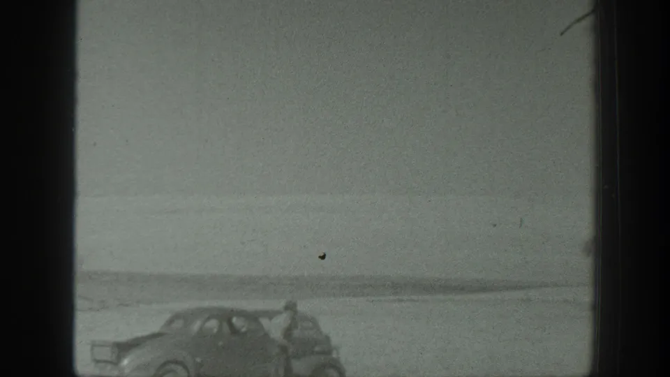 1939 California frame showing a parked period automobile and nearby travelers in a broad, empty landscape.