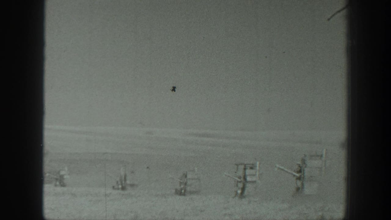 Distant row of gun-like emplacements across a flat desert plain under a hazy sky.