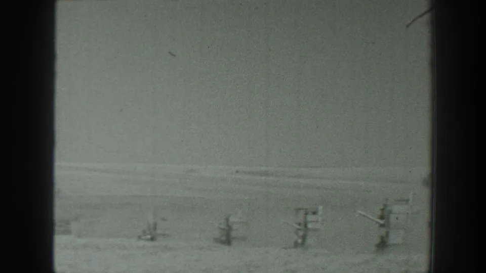 Late frame from the 1939 California clip showing a row of military-style gun emplacements across a pale desert plain.