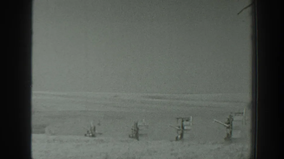 1939 California 8mm frame showing a snow-covered landscape with several indistinct distant people or structures under an overcast sky.