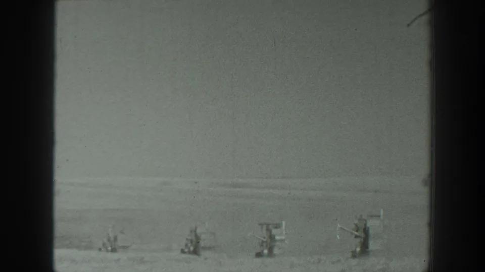 1939 California 8mm frame showing distant equipment-like structures across a flat, open landscape with soft focus and visible gate edges.