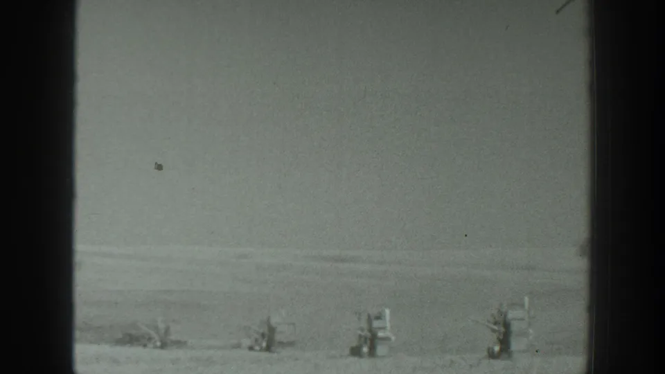 A grainy 1939 California home-movie frame with small equipment-like forms set across a distant flat landscape.