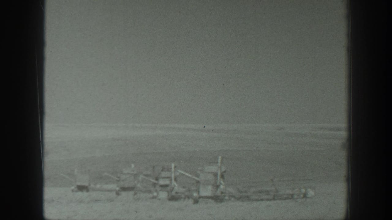 1939 California 8mm frame showing distant farm machinery across an open agricultural field under a flat sky.