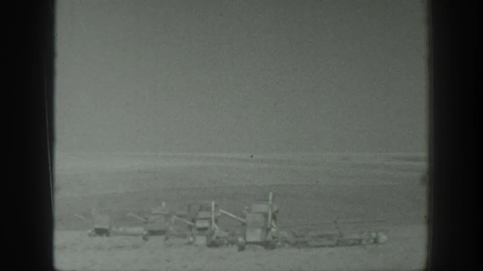 1939 California 8mm frame showing distant farm machinery across an open agricultural field under a flat sky.