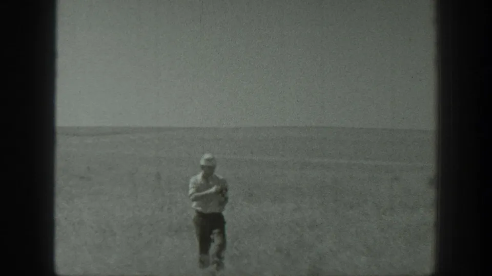 1939 California 8mm frame showing a man standing alone in an agricultural field, with a low horizon and distant hills behind him.