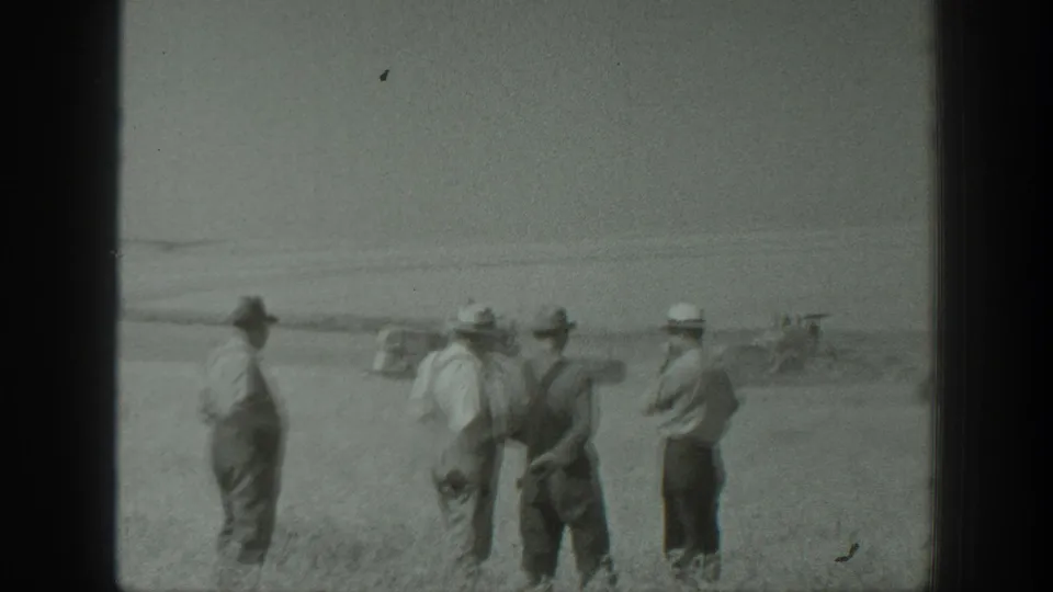 Four men in hats and work clothes stand in a California field, looking toward distant machinery or vehicles.