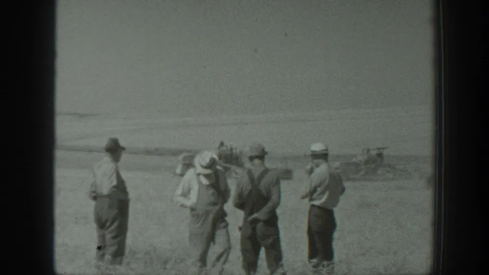 The 1939 California home-movie frame shows several men standing in a field with distant equipment beyond them.