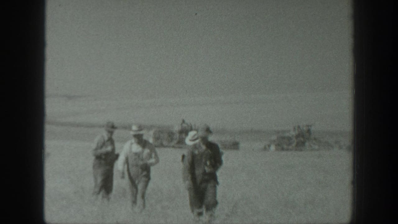 1939 California farm workers appear to walk toward the camera across a dusty field as harvesting equipment operates behind them.