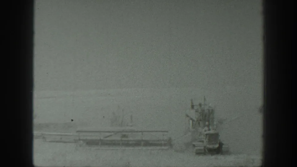 Agricultural equipment continues across a California field in 1939, with workers riding or standing on the machinery in a hazy home-movie frame.