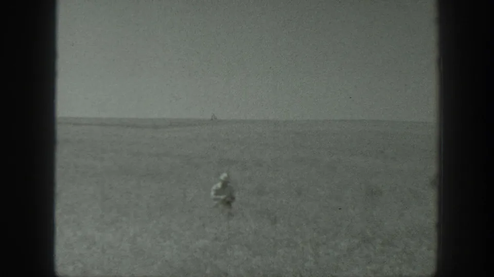 1939 California 8mm frame showing a distant person in a wide, flat field beneath an overcast sky, with soft focus and visible film grain.