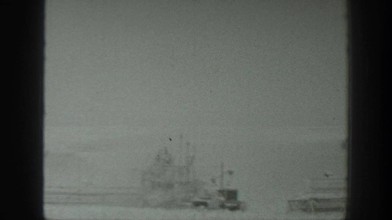 1939 California 8mm frame with low farm equipment or machinery near sparse vegetation in a broad agricultural landscape, seen through soft, grainy exposure.
