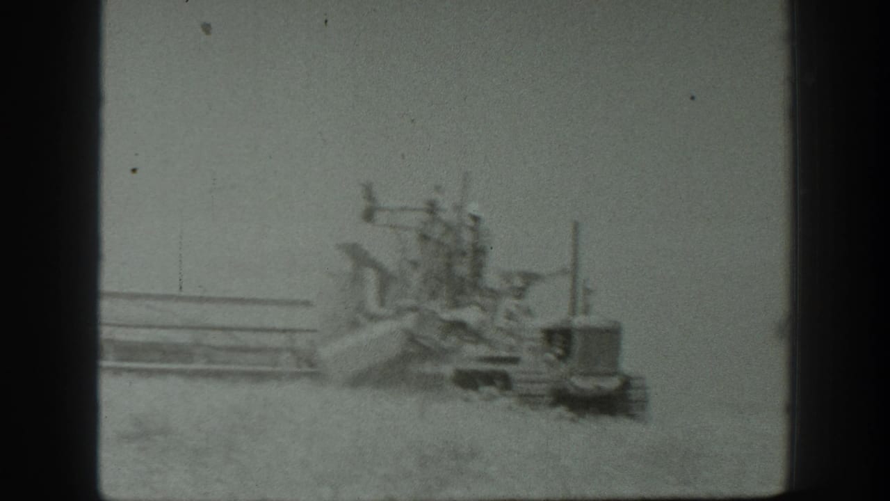 Combine harvester and tractor seen through dust in the field.