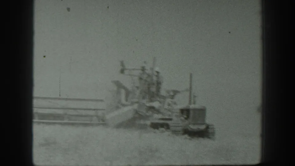 A tractor and combine harvester continue across a dusty California grain field, with workers positioned on the machinery.