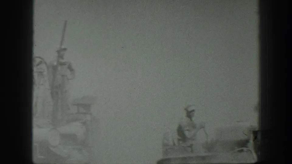 A worker is faintly visible on the combine machinery in a dusty California grain harvest scene from the 1939 home movie.