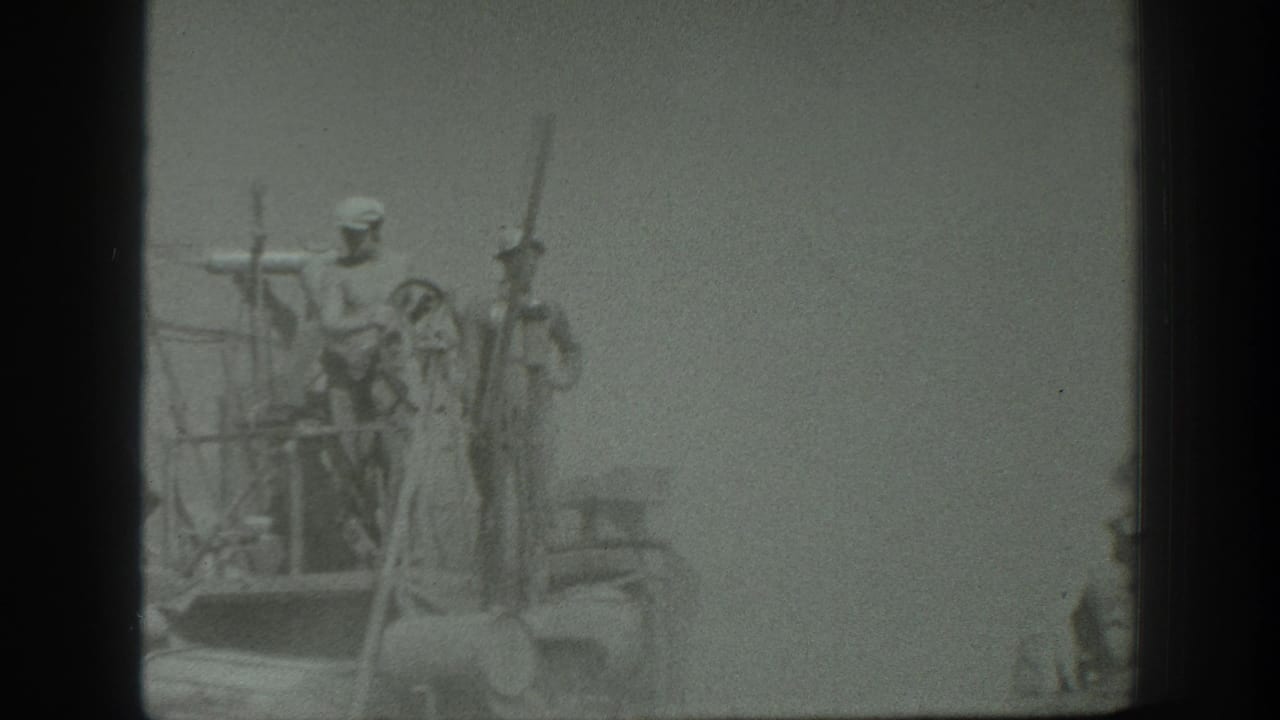 1939 California home-movie frame showing uniformed men on an elevated wooden platform with long rifle-like poles in a hazy field setting.