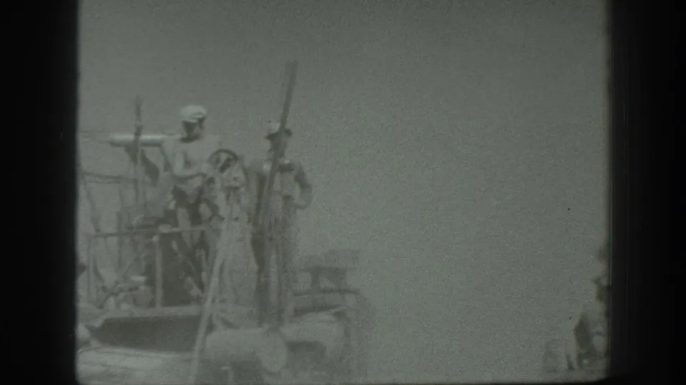 1939 California home-movie frame showing uniformed men on an elevated wooden platform with long rifle-like poles in a hazy field setting.