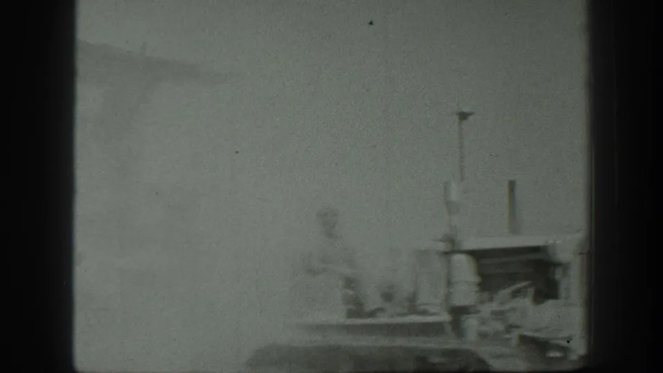 Soft 8mm frame from the California clip showing indistinct military personnel and machinery in bright haze near a platform or vehicle edge.