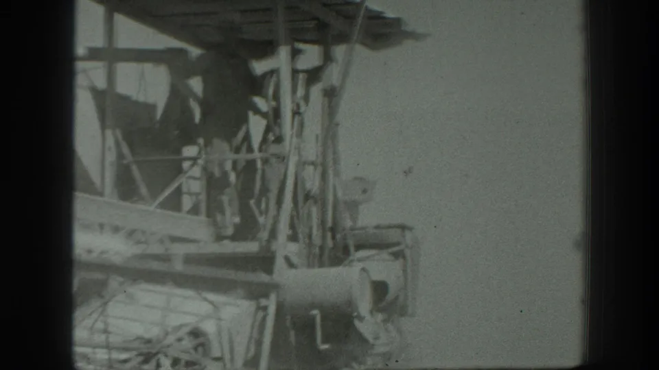 Final 8mm frame shows uniformed personnel near a wooden-framed machine or cart, with wheels, supports, and a cylindrical component visible.