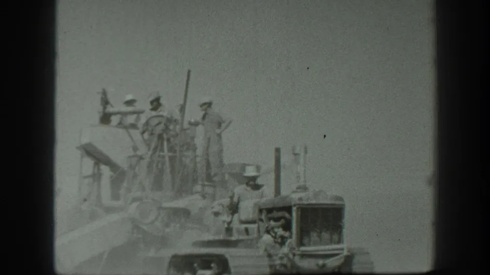 In 1939 California home-movie footage, a tractor driver appears near several men standing on a large field cutter.