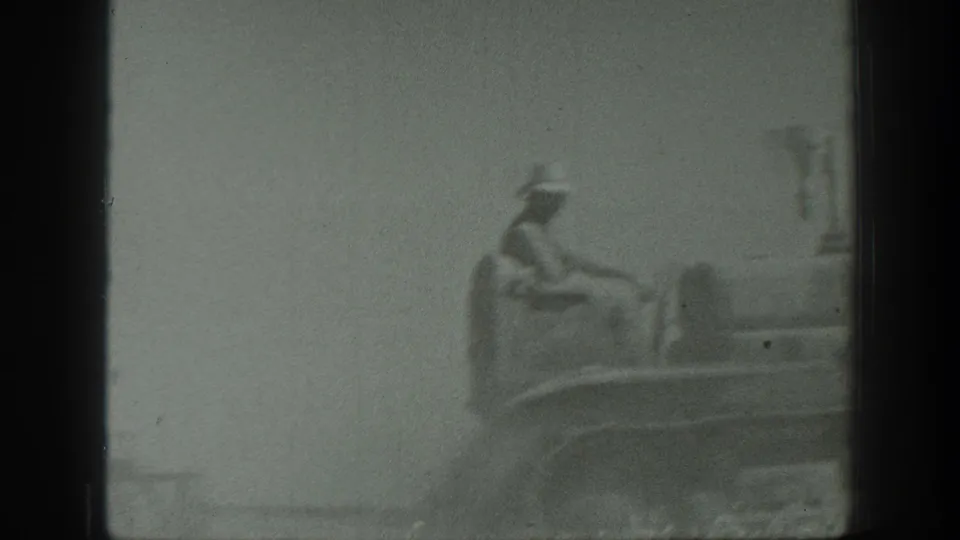 A hat-wearing tractor driver is partly visible through dust and soft focus in this 1939 California farm footage.