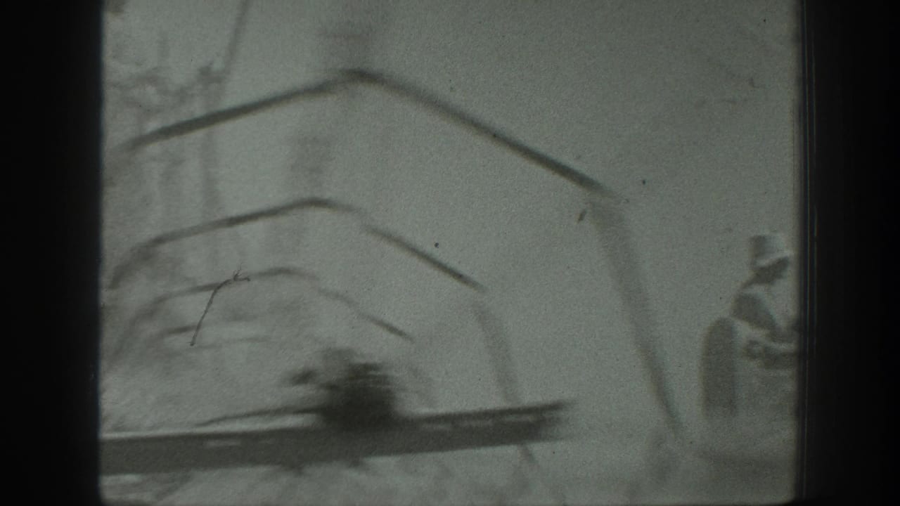 Soft black-and-white frame with farm machinery partly obscured by film borders and a worker at the right edge.
