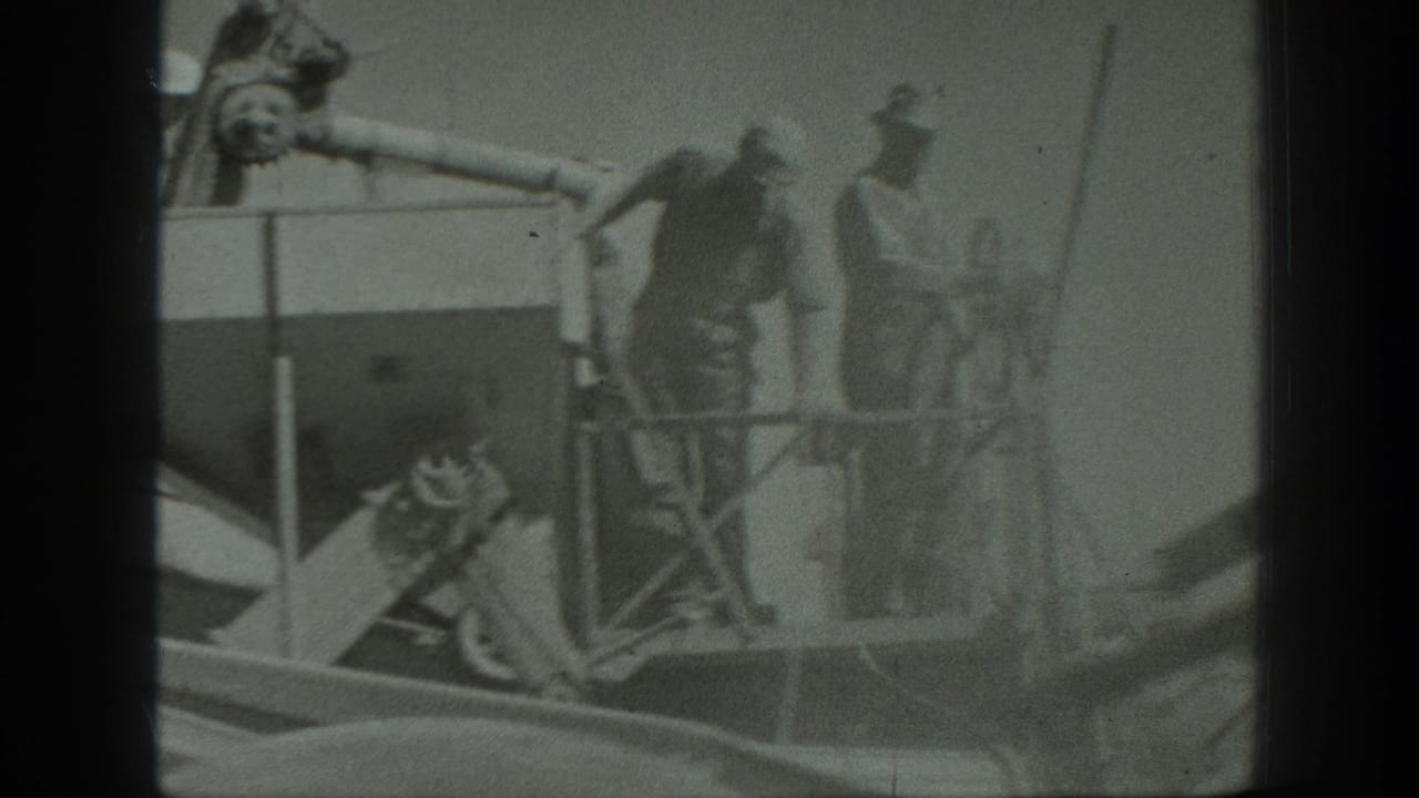 Several men stand on and near a large threshing machine with exposed mechanical parts in a field.
