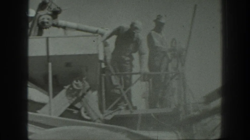 1939 California harvest scene with men in hats standing on and around a large threshing machine in an open wheat field.