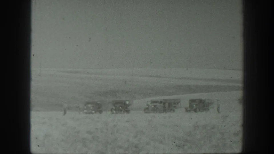 Wide 1939 California field view showing several distant parked vehicles near the harvest area, with open land and sky beyond.
