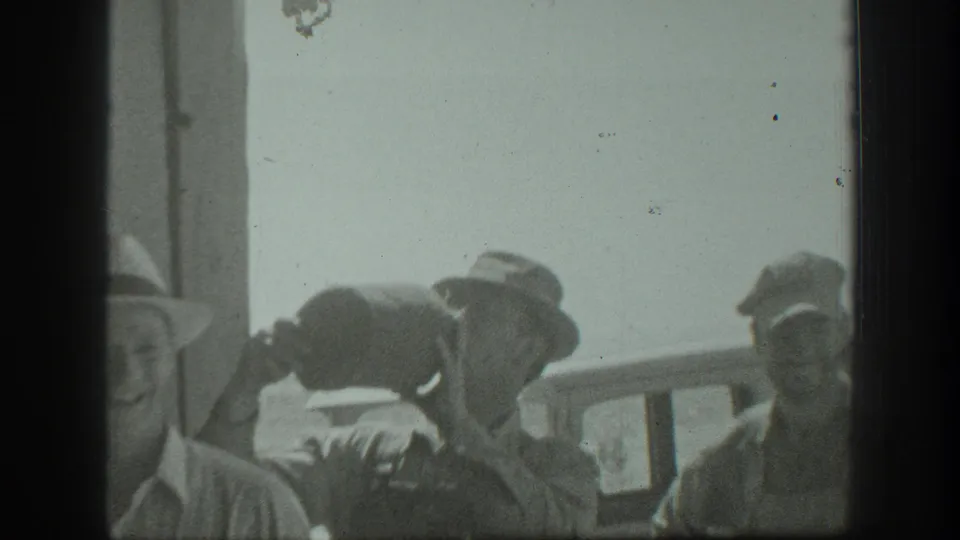A sunlit 1939 California home-movie frame shows adult men near a railing, with one man raising a large jug to drink.