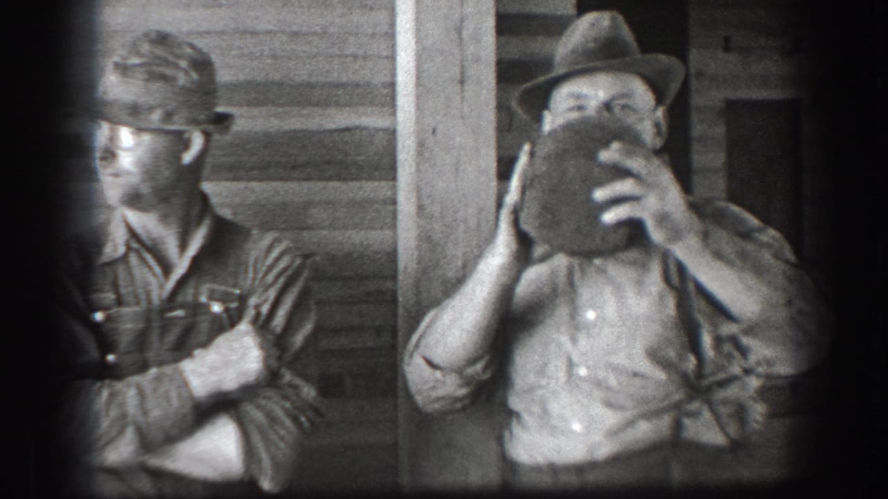 Two adult men in hats stand beside a wooden porch wall.