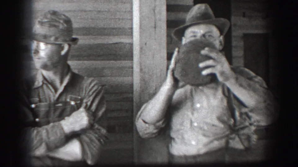 Two adult men in hats and work clothes stand by a wooden porch in 1939 California home-movie footage.
