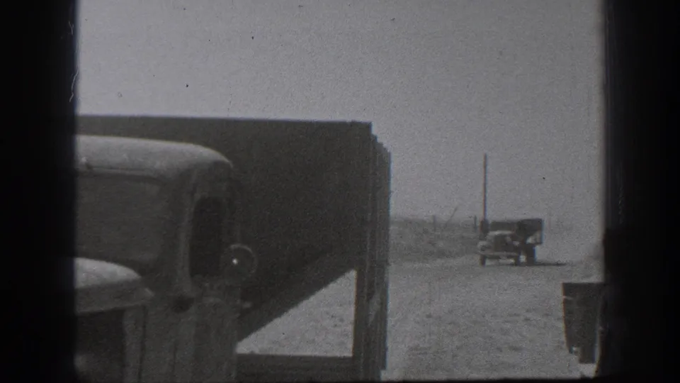 A dusty California road scene shows a truck and distant vehicles in black-and-white 1939 home-movie footage.