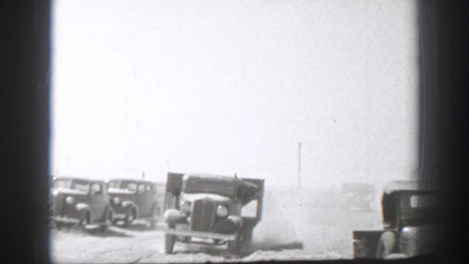 1939 California 8mm frame showing boxy military-style trucks in a dusty open area, seen through dark foreground borders.