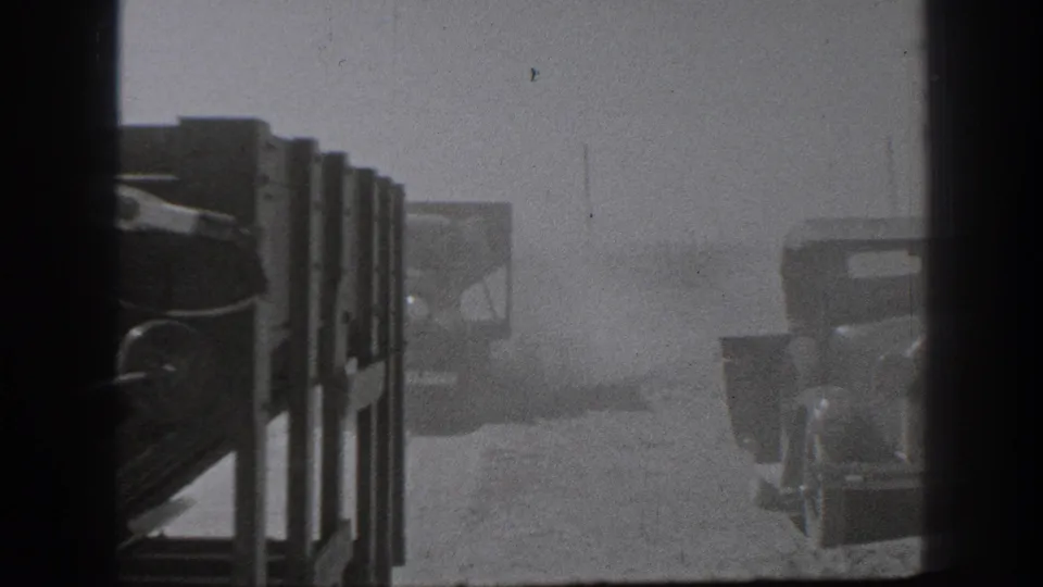 1939 California 8mm frame with military-style trucks in a dusty field, viewed through dark foreground borders and haze.