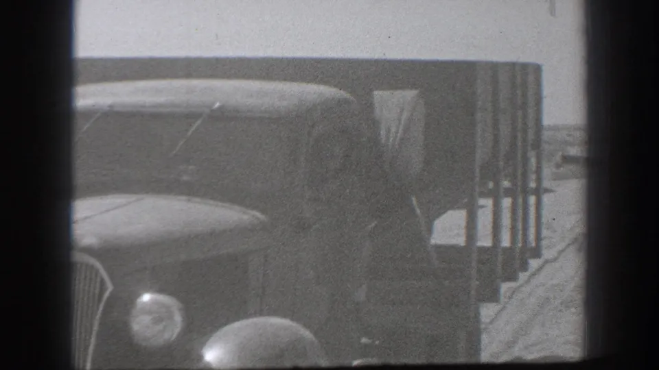 1939 California 8mm close frame of a military-style truck body and front fender, with other dusty vehicles nearby.