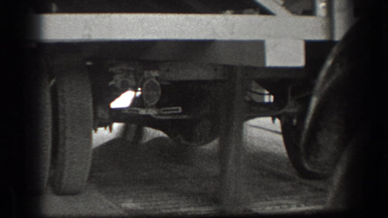 Low-angle view beneath a vintage truck, showing wheels, axle, suspension, and dark film edges.
