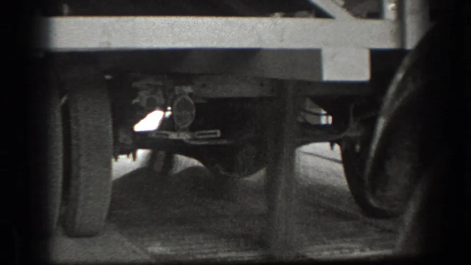 Low-angle 1939 California 8mm frame showing the underside of a vintage truck with wheels, axle, suspension parts, road surface, and shadowed film edges.