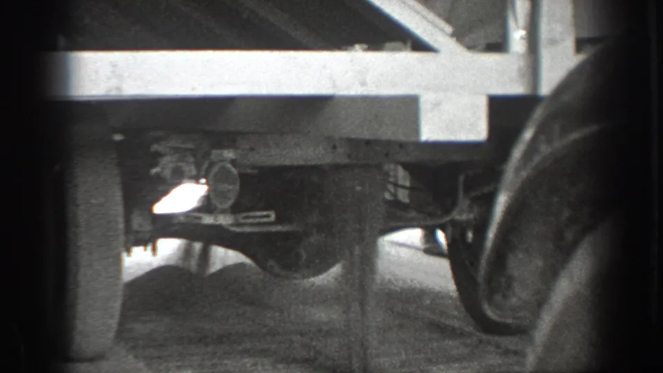 Low-angle 1939 California home-movie frame of a truck underside, with axle hardware, wheels, dusty road surface, and a dark foreground obstruction.