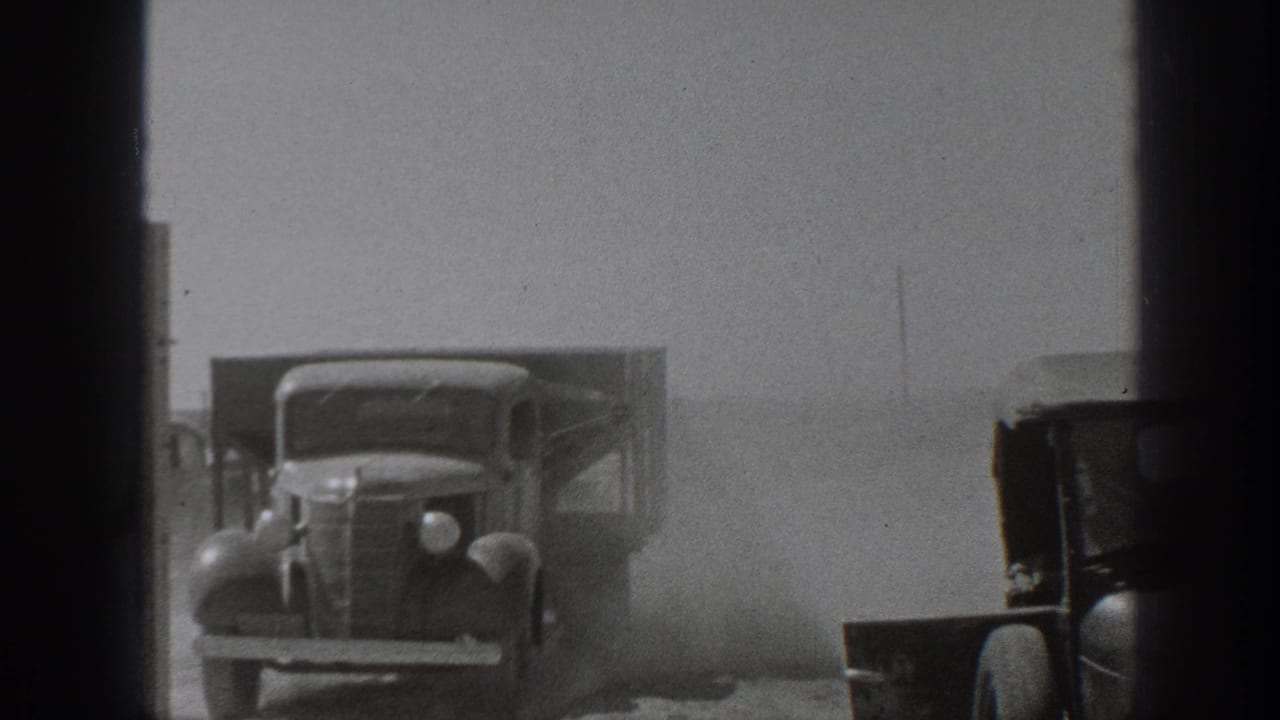 1939 California home-movie frame showing classic trucks in a dusty work area, partly obscured by dark gate edges.
