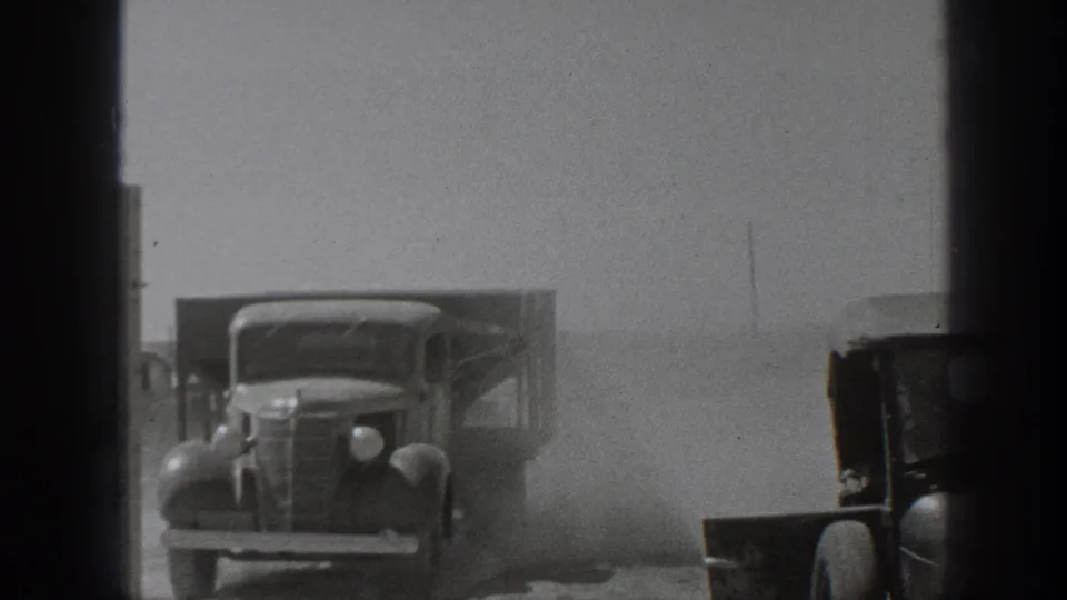 1939 California home-movie frame showing classic trucks in a dusty work area, partly obscured by dark gate edges.