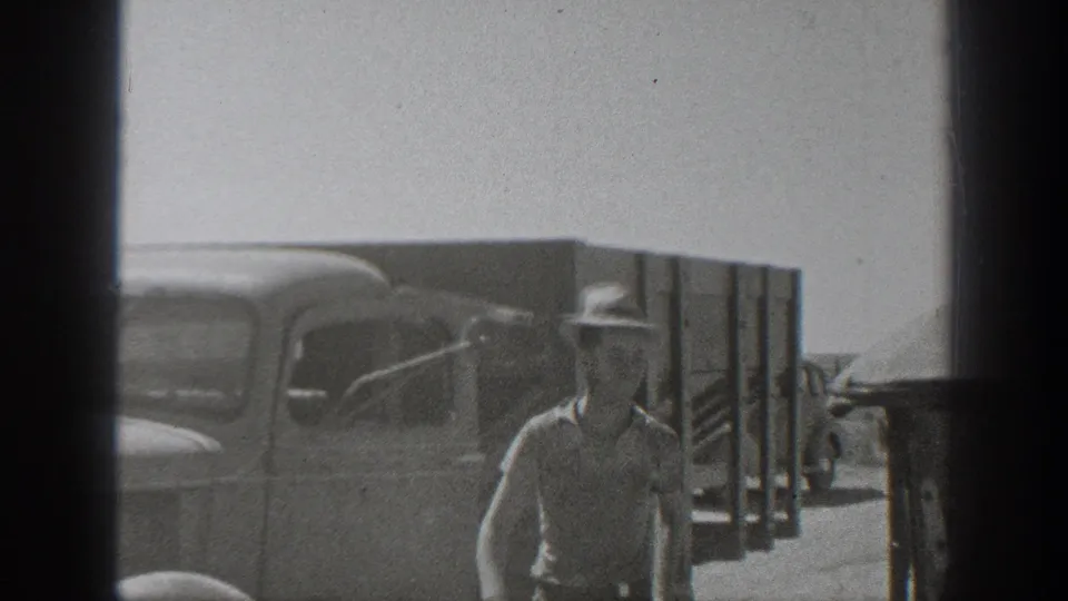 A man in work clothes and a hat approaches the camera near a classic truck in this 1939 California home-movie frame.
