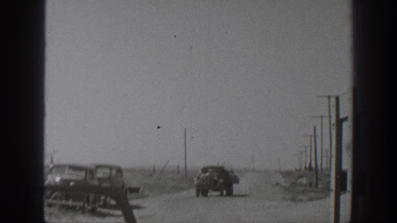 1939 California home-movie frame showing automobiles on a dusty rural road lined with utility poles.