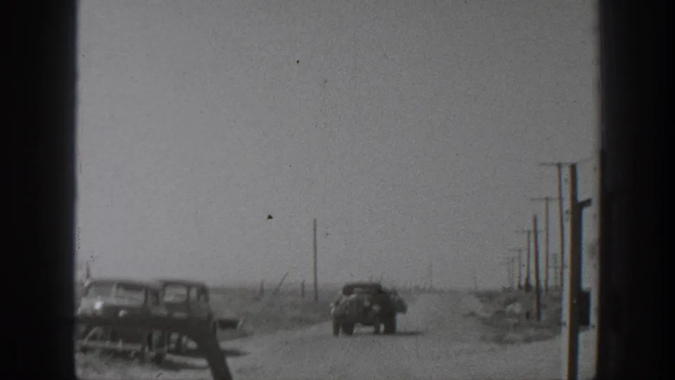 1939 California home-movie frame showing automobiles on a dusty rural road lined with utility poles.