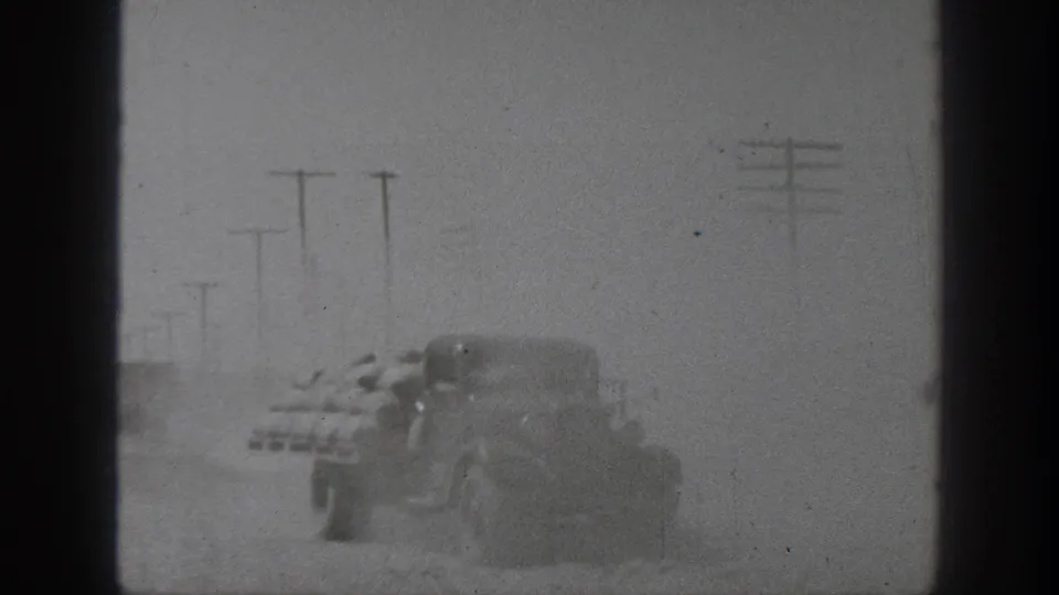 A vintage vehicle carrying stacked sacks drives through dust on a California rural road in 1939 footage.