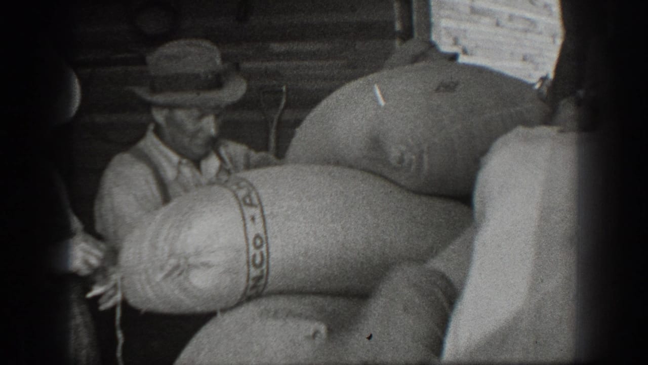 1939 California 8mm frame showing a man in a brimmed hat near large PANCO-marked burlap sacks in a rustic storage area.