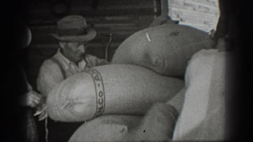 1939 California 8mm frame showing a man in a brimmed hat near large PANCO-marked burlap sacks in a rustic storage area.